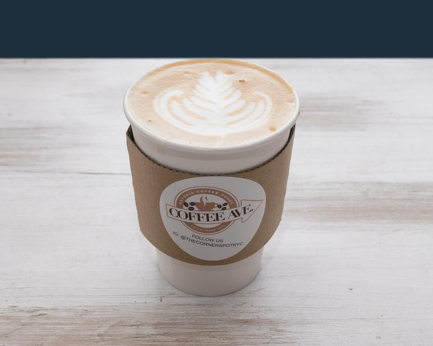 Latte with rosetta art in a Coffee Ave kraft sleeve